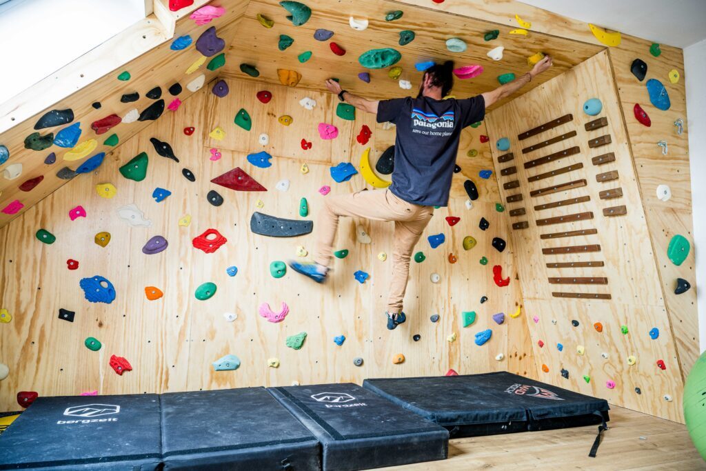 Klimmer bouldert op de afgewerkte zoldermuur met campusboard en valmatten