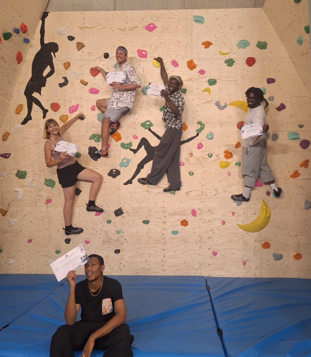 IMG-20260812-WA0005 Vijf deelnemers poseren met hun certificaat op de bouldermuur na de opleiding boulderen bij VZW Erat