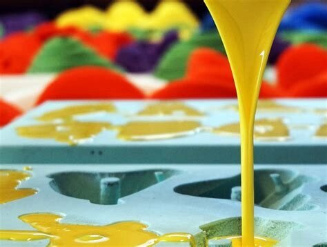 Gele vloeibare polyurethaanhars wordt in blauwe siliconenmallen voor klimgrepen gegoten, met afgewerkte gekleurde grepen op de achtergrond